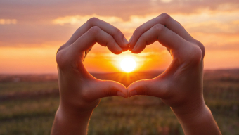 Framing the Moment: Heart-Shaped Hands Against a Glowing Sunrise