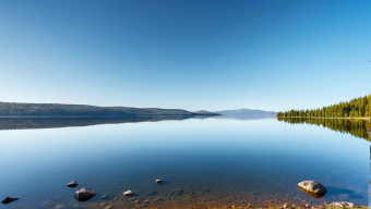 Tranquil Lakeside Landscape with Forested Hills and Clear Blue Sky